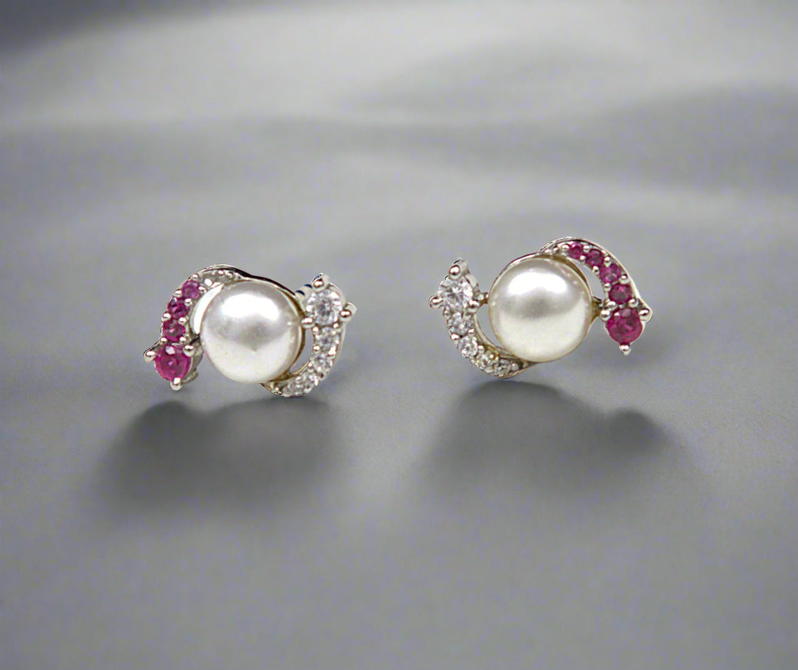 Pair of pearl earrings with red gemstones on a textured white background
