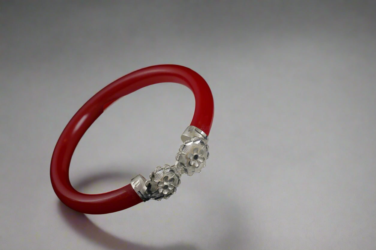 Red bracelet with silver clasp on a white stand against a black background