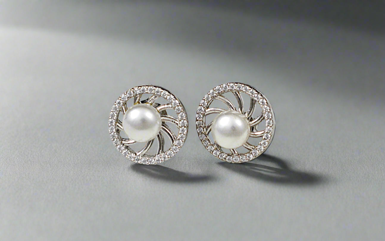 Pair of pearl earrings with silver and crystal accents on a textured white surface