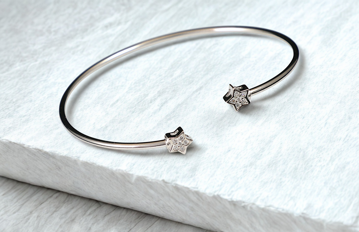 Silver bracelet with star-shaped charms on a white marble surface