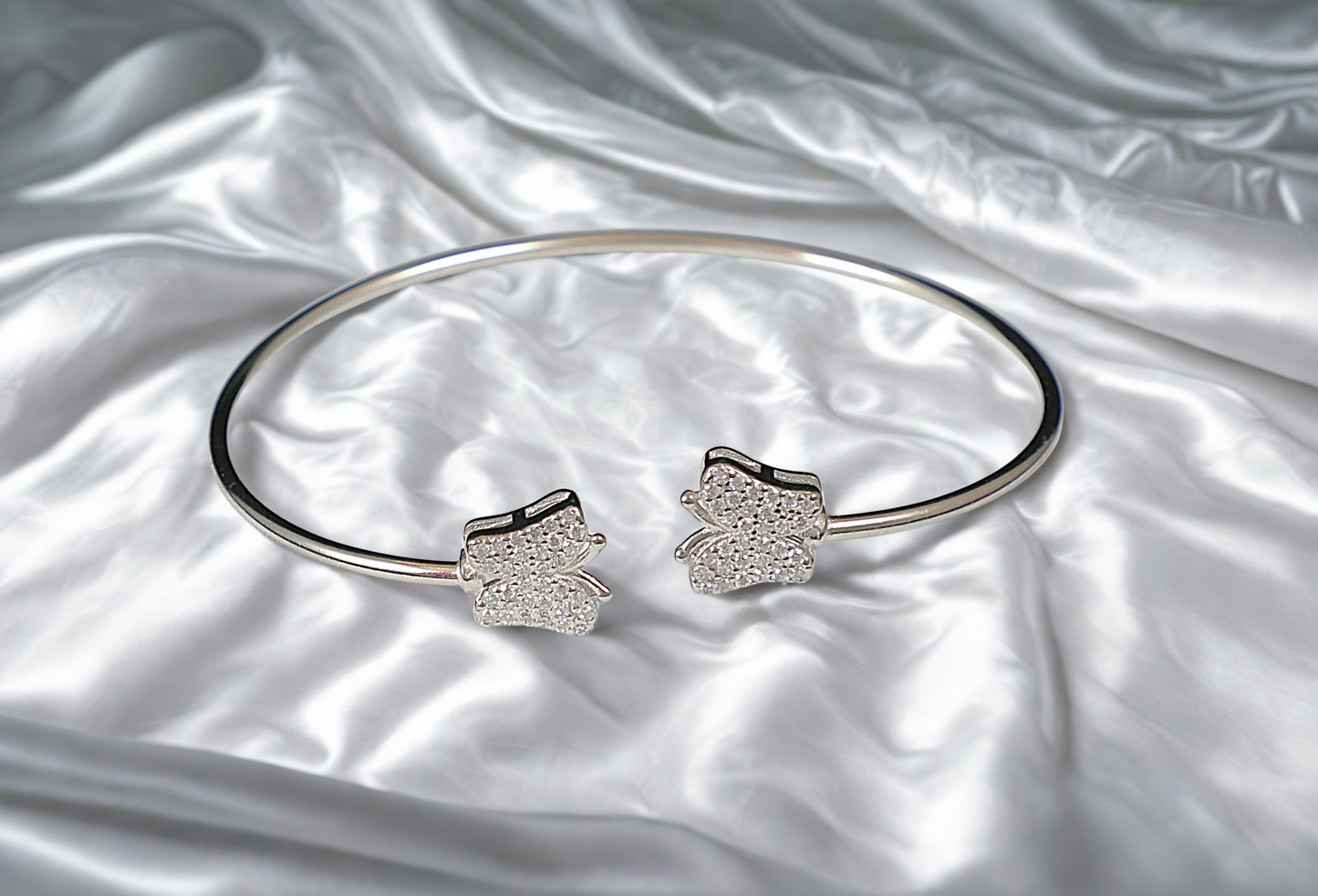 Silver bracelet with butterfly-shaped ends on a satin surface