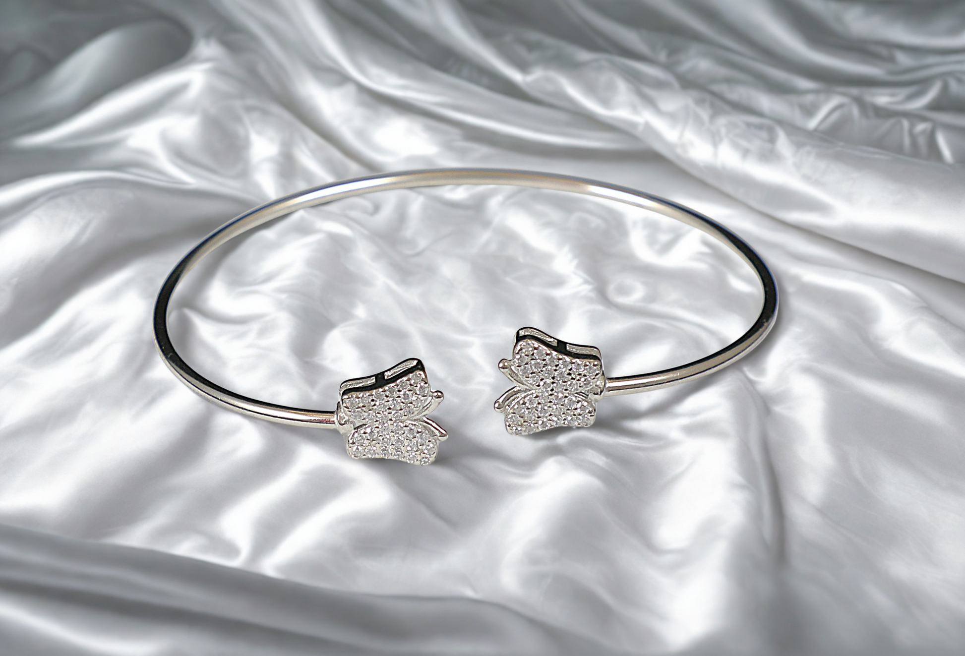 Silver bracelet with butterfly-shaped ends on a satin surface