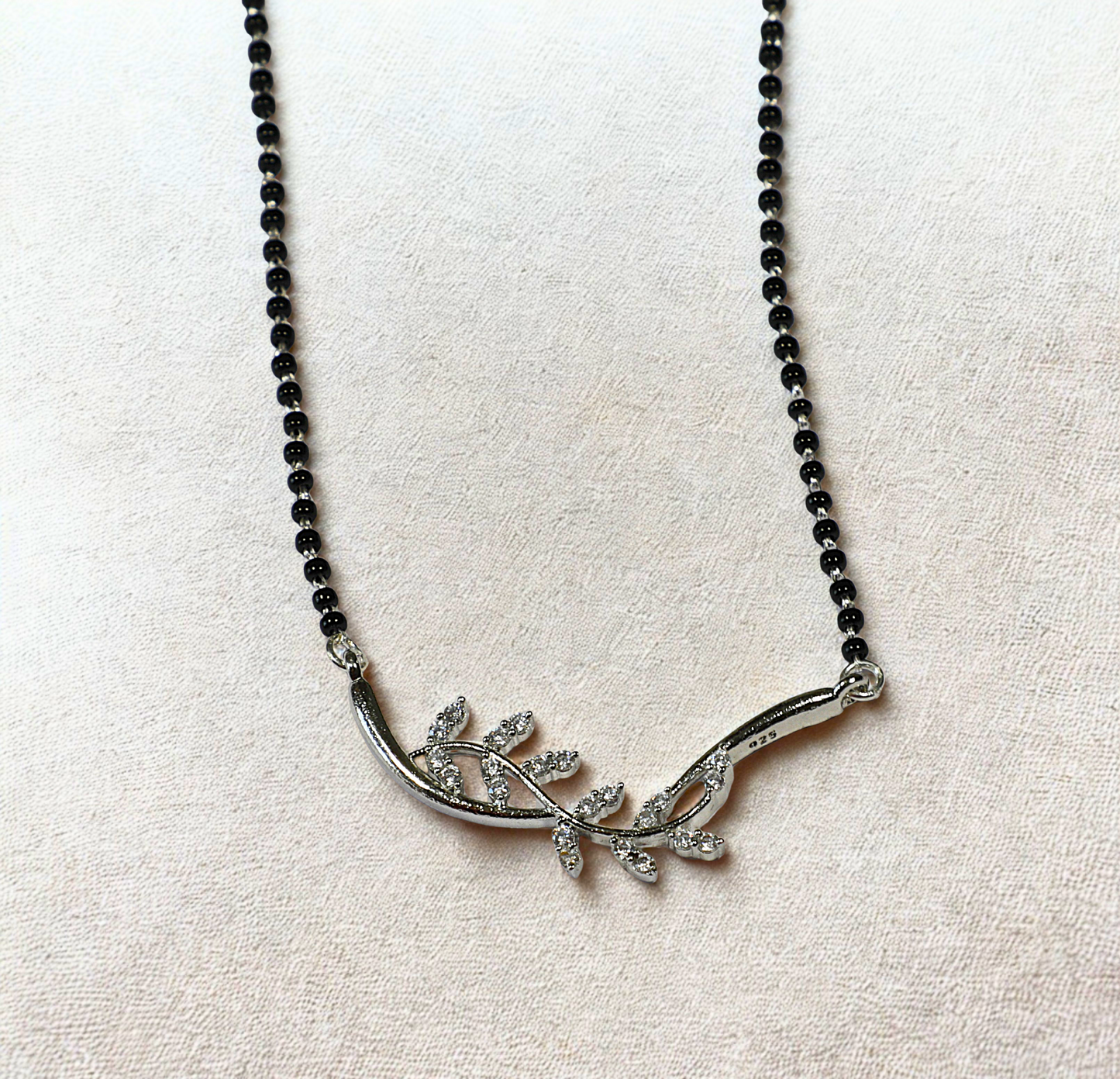 Silver leaf-shaped pendant on a black beaded necklace against a light fabric background