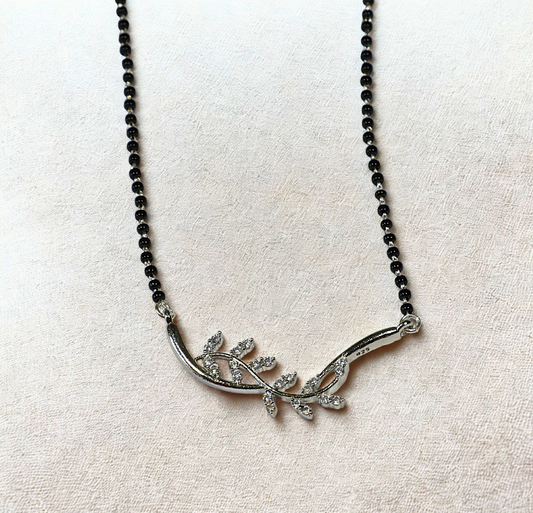 Silver leaf-shaped pendant on a black beaded necklace against a light fabric background