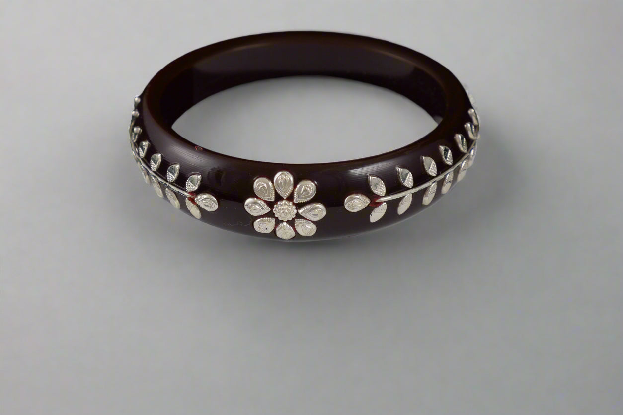 Brown bangle with floral patterns on a white stand against a black background