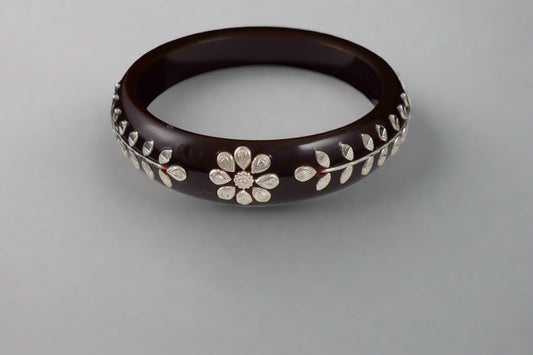 Brown bangle with floral patterns on a white stand against a black background