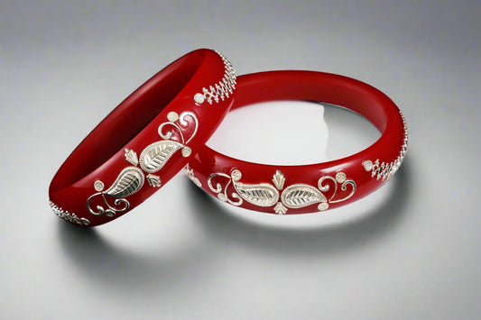 Two red bangles with silver designs on a white stand against a black background