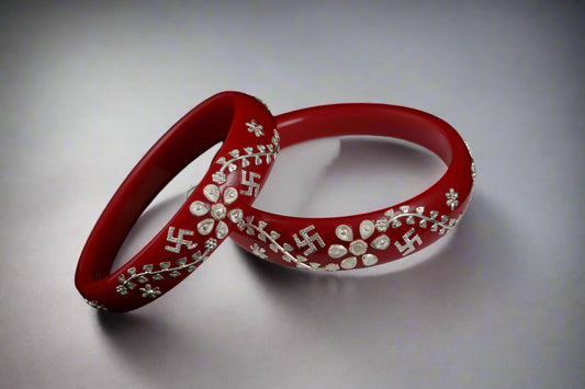 Red bangles with silver swastika design on a white stand against a black background