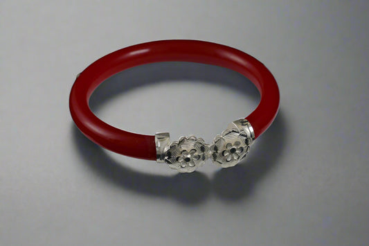 Red bracelet with silver charms on a white stand against a black background