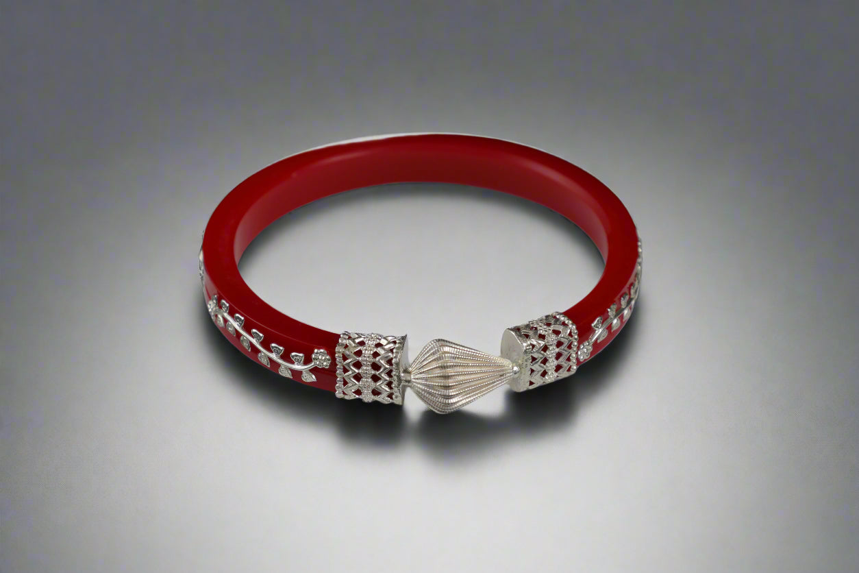Red bracelet with silver charms on a white stand against a black background