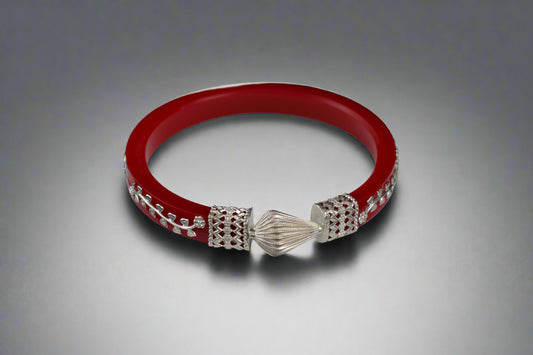 Red bracelet with silver charms on a white stand against a black background