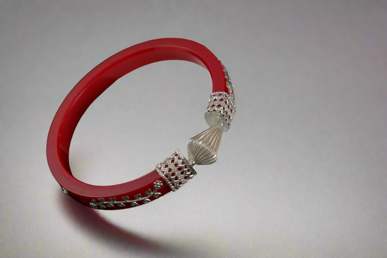 Red bracelet with silver beads on a white hexagonal stand against a black background