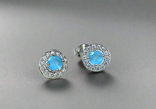 Pair of silver earrings with blue gemstones on a white marble background