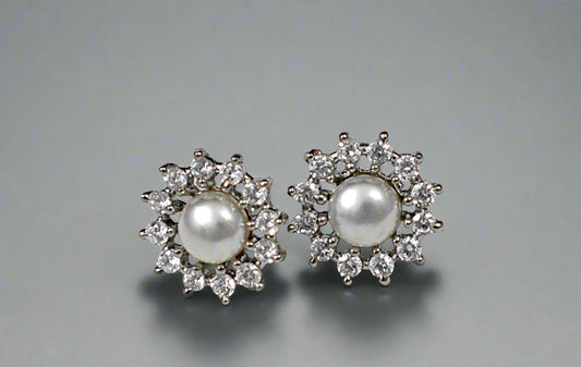 Pair of pearl earrings with diamond accents on a textured gray background