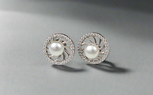 Pair of pearl earrings with silver and crystal accents on a textured white surface