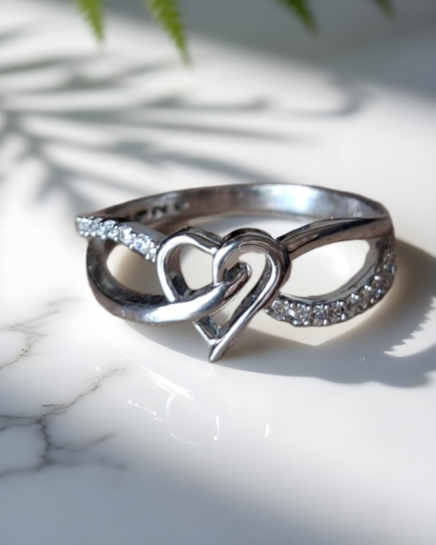 Silver ring with heart and infinity design on a marble surface