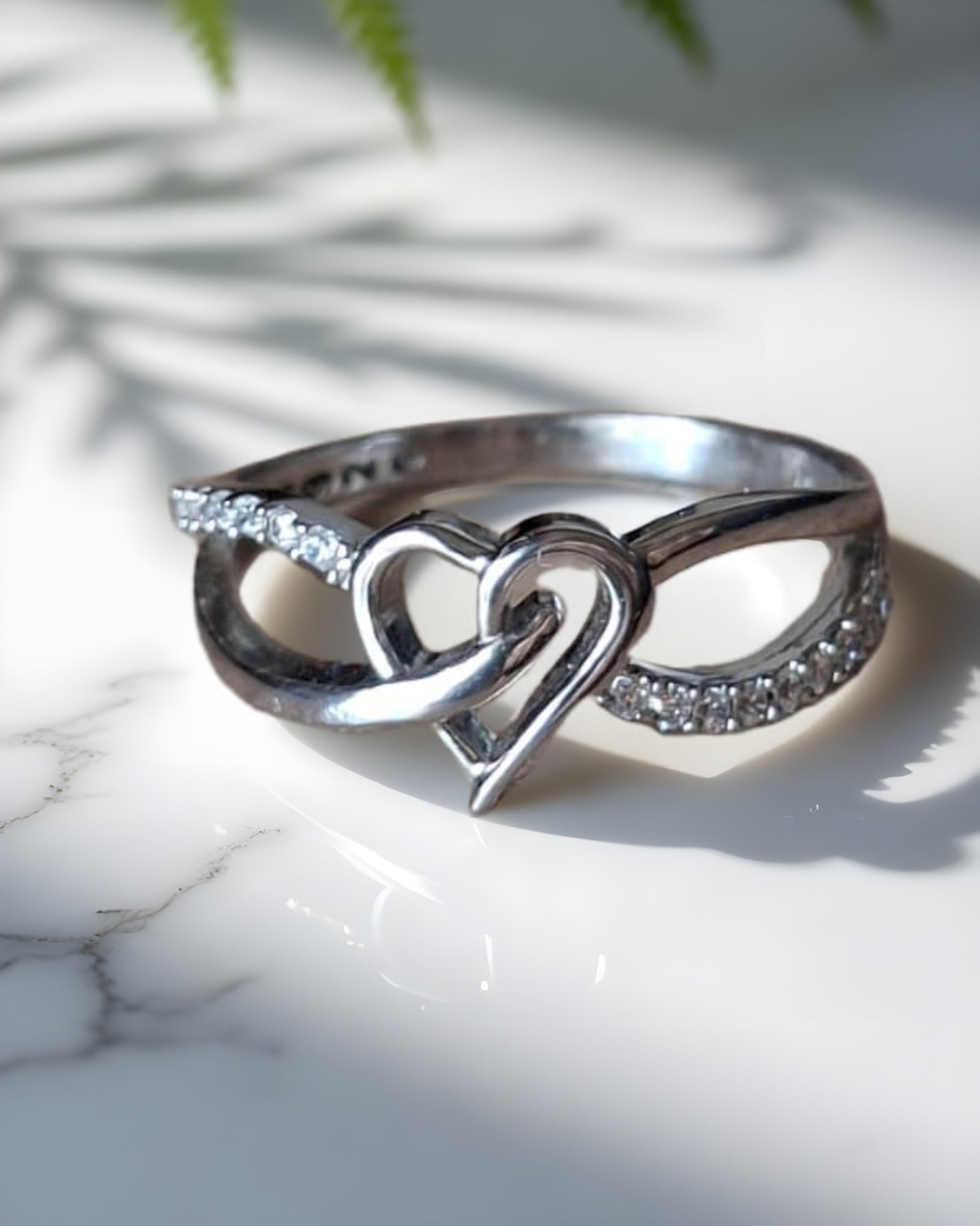 Silver ring with heart and infinity design on a marble surface