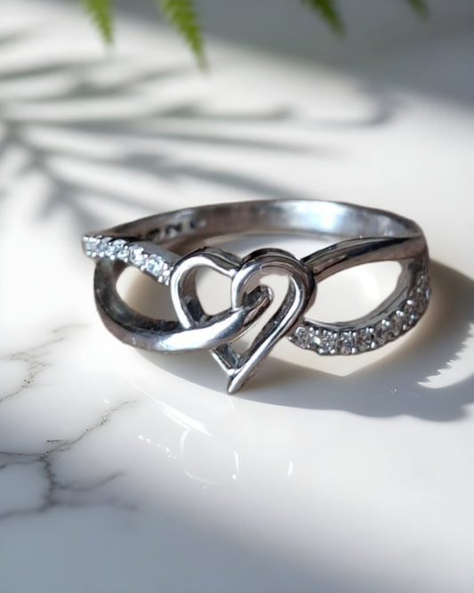 Silver ring with heart and infinity design on a marble surface